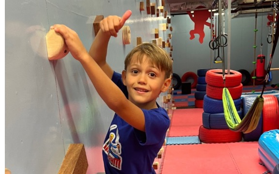 A boy on the NinjaGym climbing wall giving a thumbs up