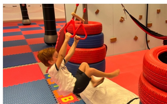 A boy swinging on the trapeze over the tire obstacles