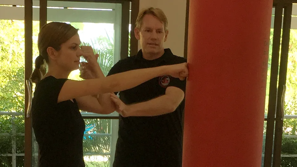 Rick Tew guiding a woman's straight punch into a standing bag