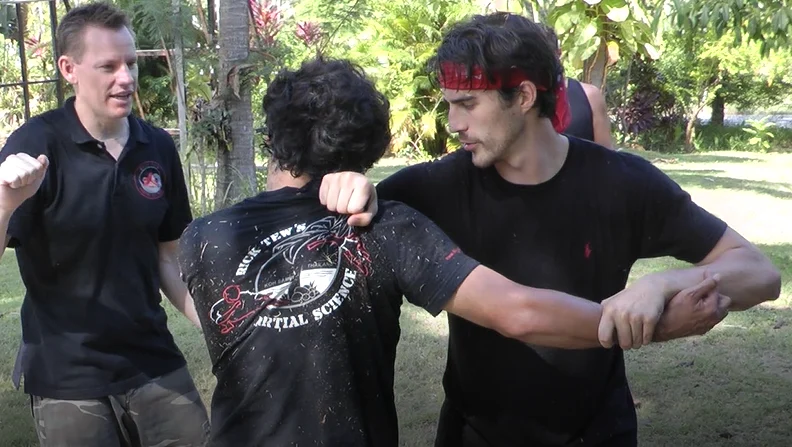 Rick Tew, in a black shirt, coaching two students through an arm technique outdoors